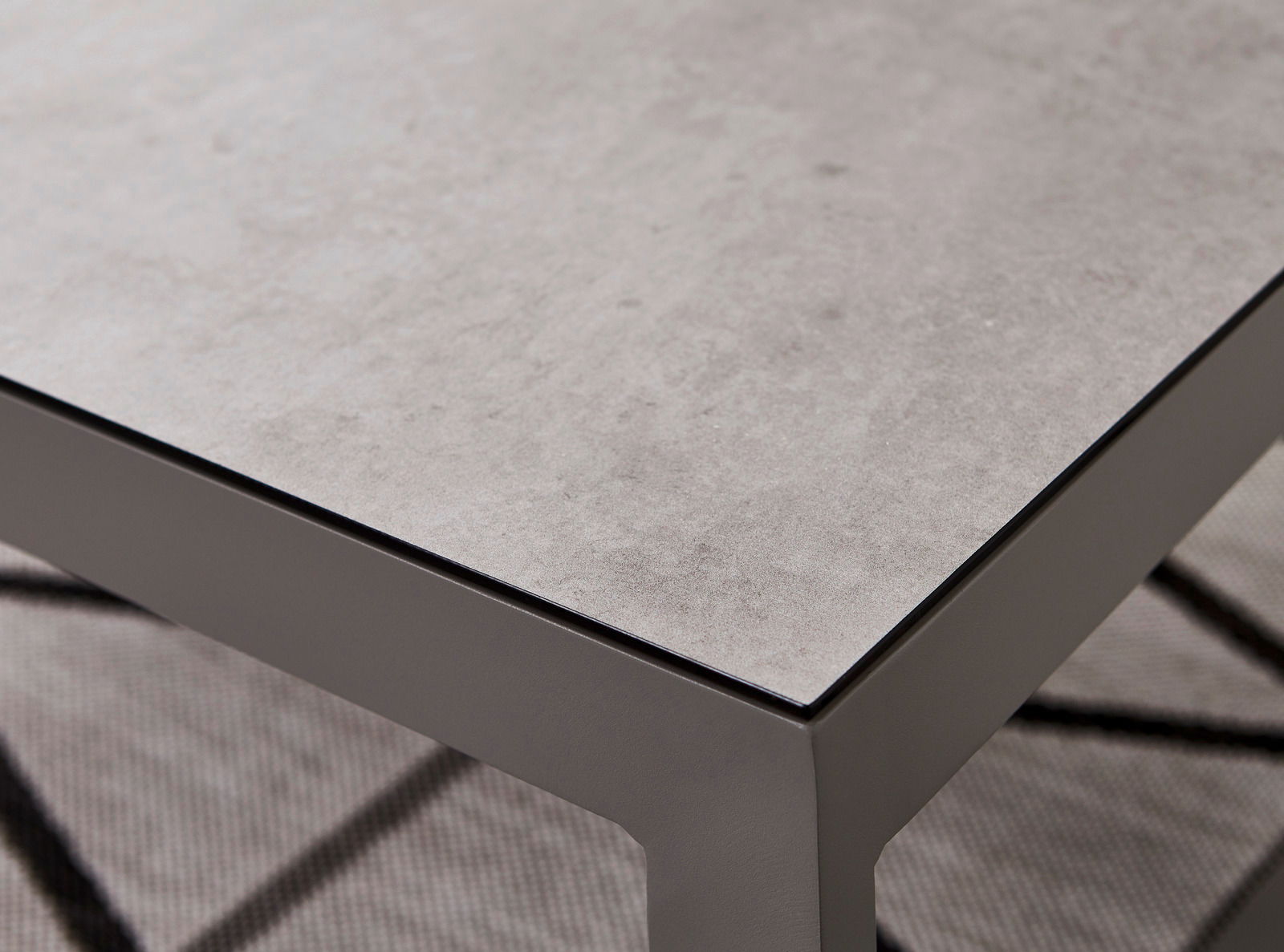 Nahaufnahme eines modernen Lounge-Tisches mit grauer Steinoptik-Oberfläche und stabilen Metallbeinen, perspektivisch von oben fotografiert.