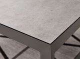 Nahaufnahme eines modernen Lounge-Tisches mit grauer Steinoptik-Oberfläche und stabilen Metallbeinen, perspektivisch von oben fotografiert.