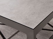 Nahaufnahme eines modernen Lounge-Tisches mit grauer Steinoptik-Oberfläche und stabilen Metallbeinen, perspektivisch von oben fotografiert.