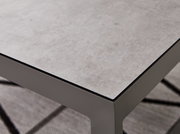 Nahaufnahme eines modernen Lounge-Tisches mit grauer Steinoptik-Oberfläche und stabilen Metallbeinen, perspektivisch von oben fotografiert.