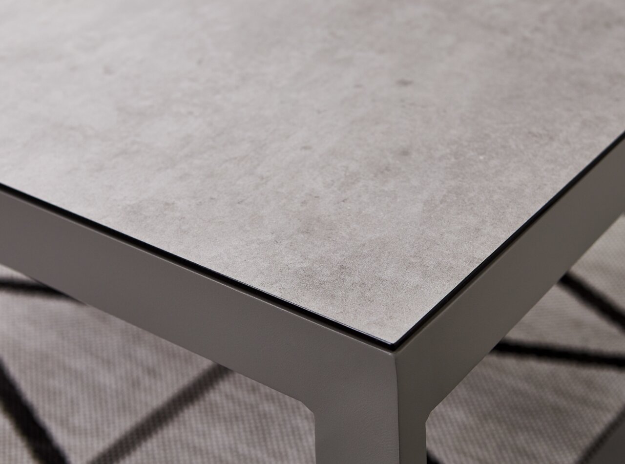 Nahaufnahme eines modernen Lounge-Tisches mit grauer Steinoptik-Oberfläche und stabilen Metallbeinen, perspektivisch von oben fotografiert.