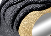 Nahaufnahme eines Spiegels mit strukturiertem, wellenförmigem Rahmen in Schwarz und Gold, aus seitlicher Perspektive.
