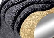 Nahaufnahme eines Spiegels mit strukturiertem, wellenförmigem Rahmen in Schwarz und Gold, aus seitlicher Perspektive.