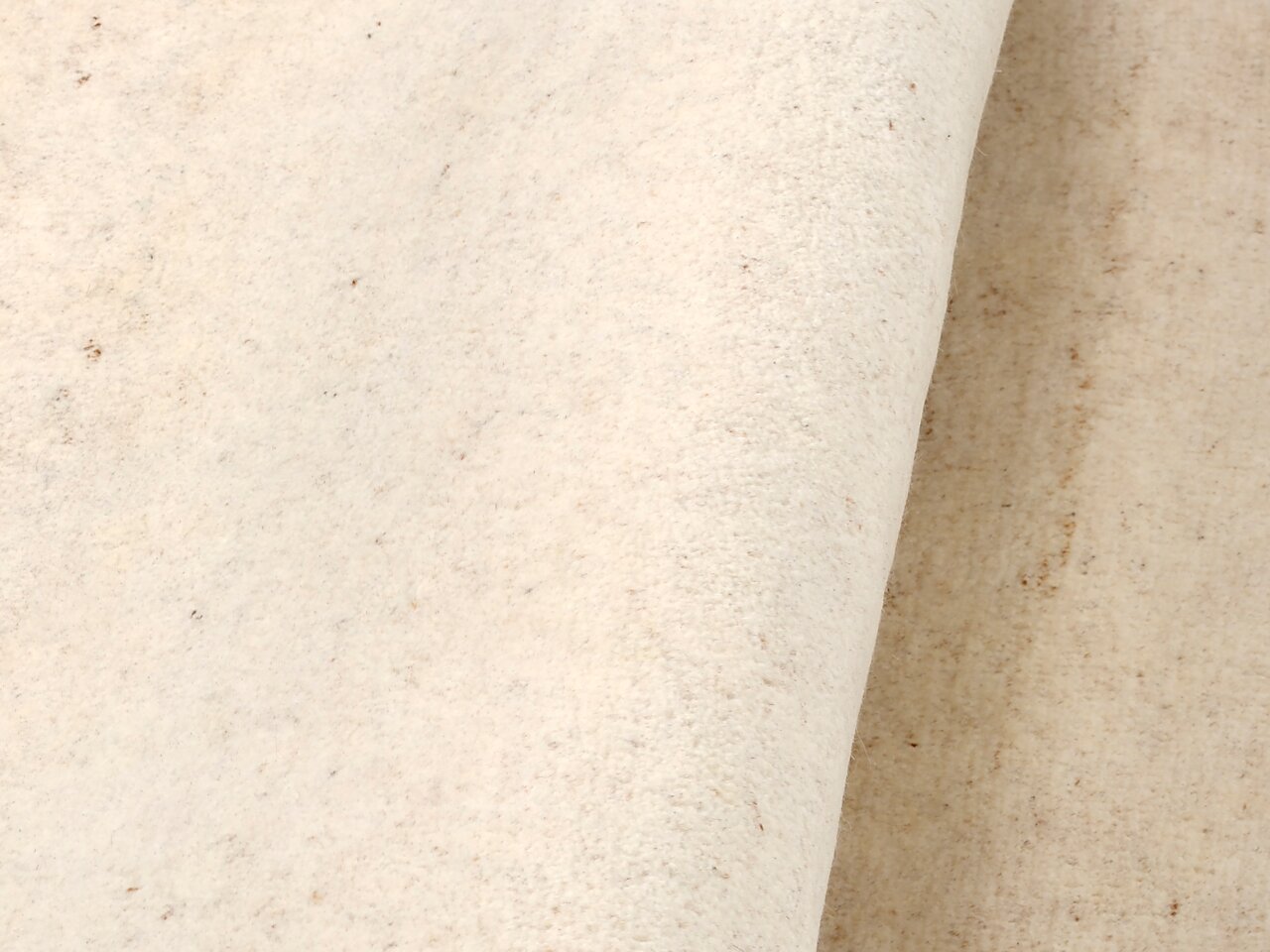 Nahaufnahme eines cremefarbenen Wollteppichs mit leichter Textur, seitliche Perspektive