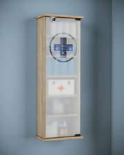 Schmaler abschließbarer Medizinschrank aus Holz mit milchiger Glastür und Kreuzsymbol, gefüllt mit Erste-Hilfe-Artikeln, schräg von vorne links an der Wand gezeigt