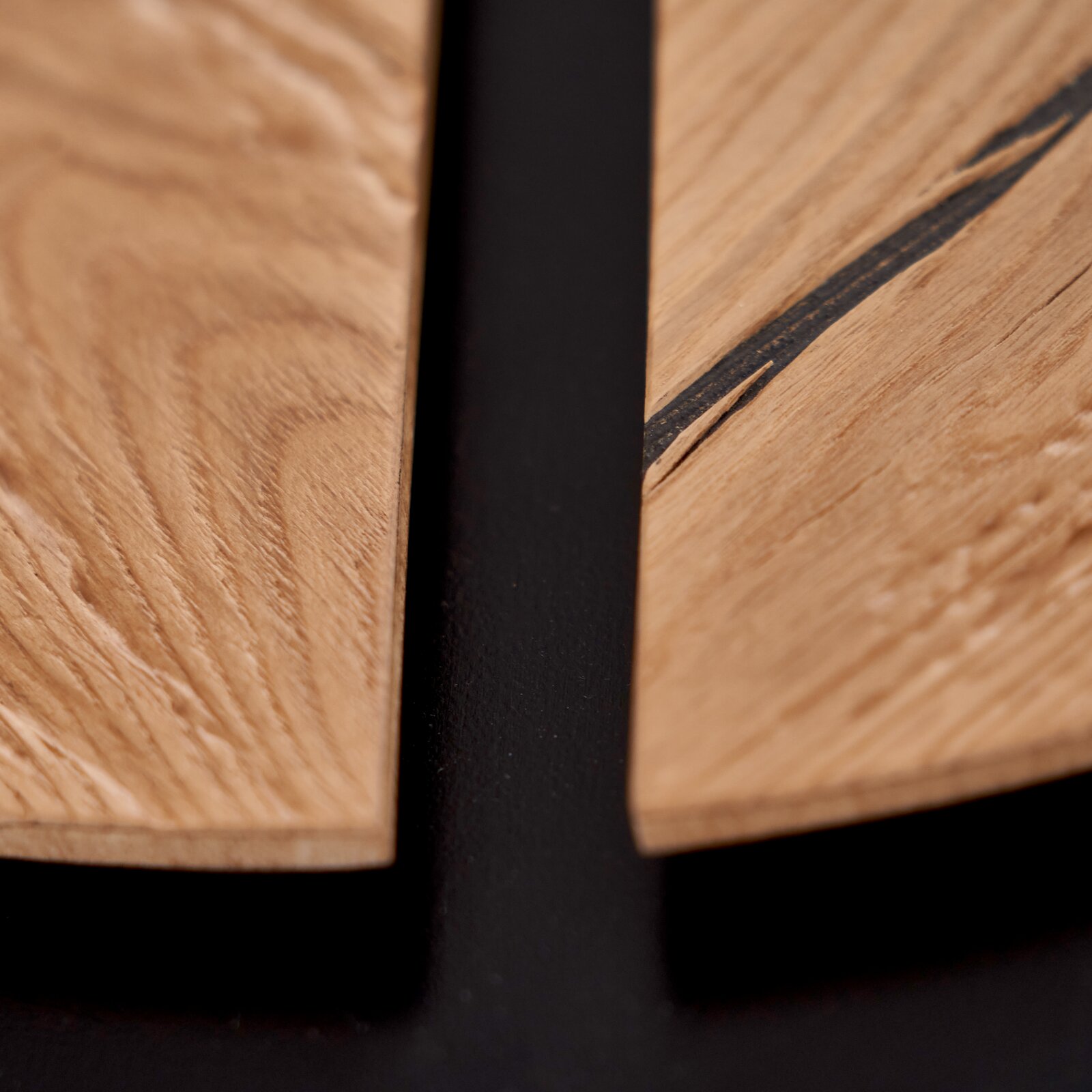 Detailansicht aus der Vogelperspektive auf zwei natürlich gemaserte Holzplatten mit schwarzem Metallrahmen und dunkler Harzeinlage