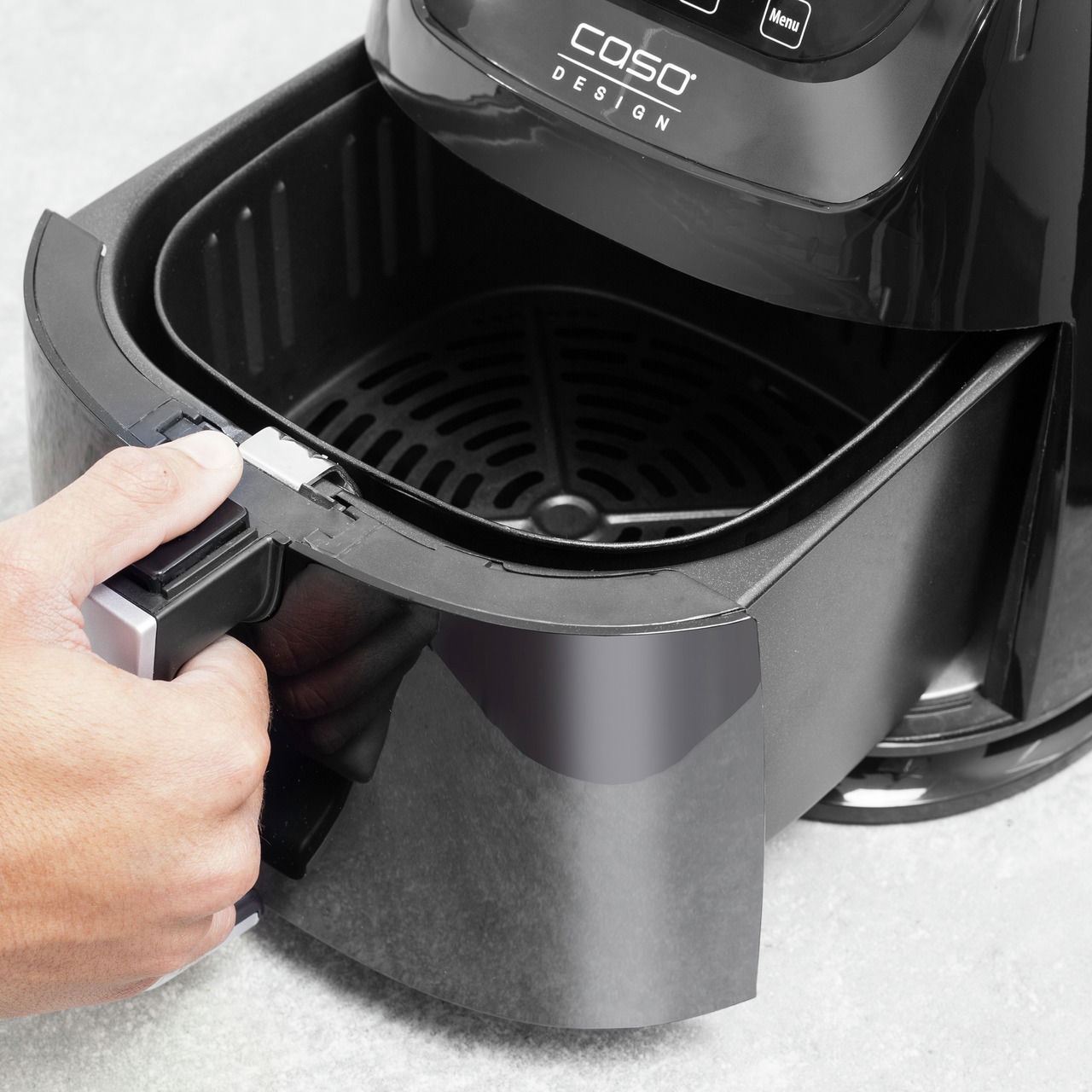 Nahaufnahme einer schwarzen Heißluftfritteuse mit geöffneter Schublade, die von einer Hand gehalten wird.