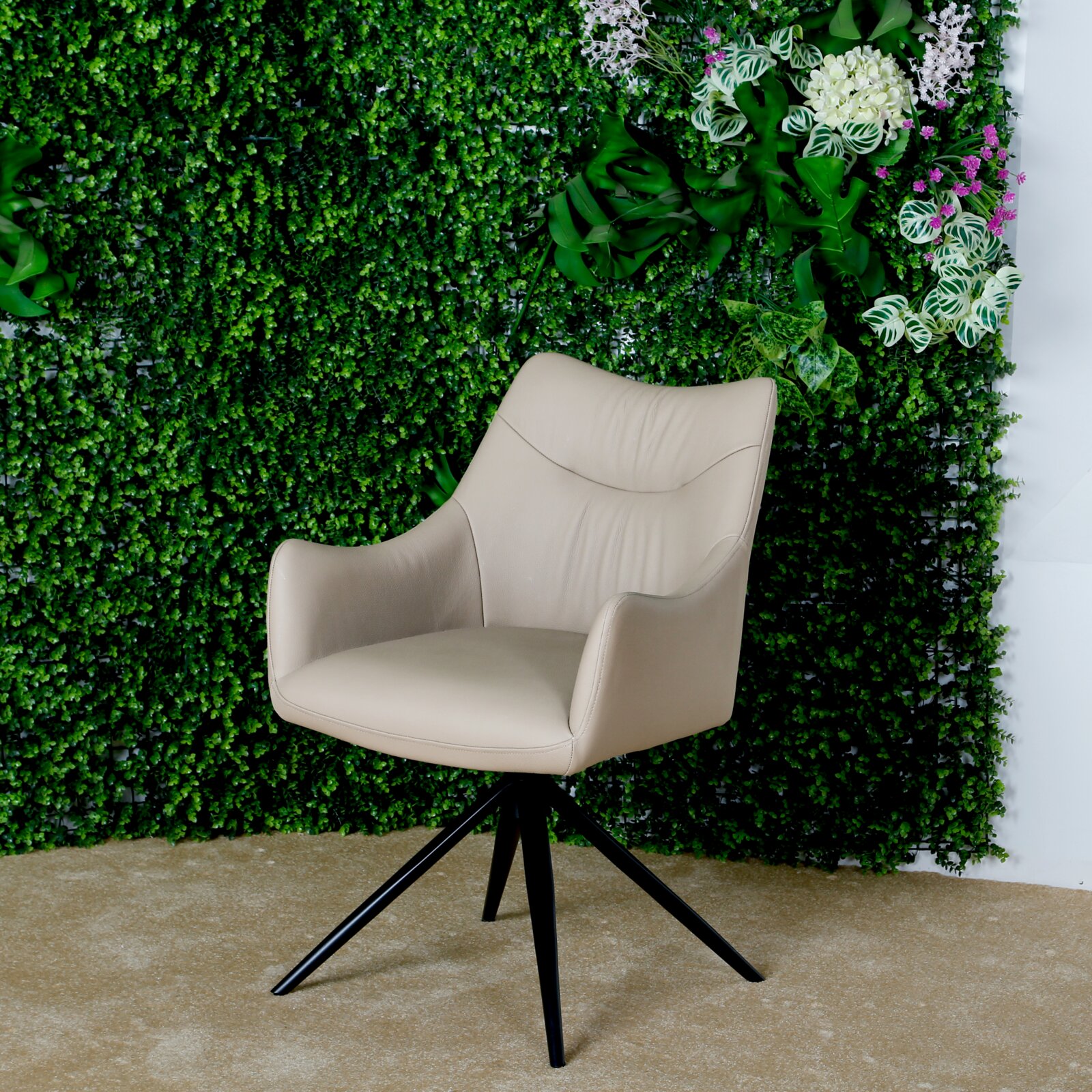 Beige fauteuil met zwart metalen frame, voor een groene plantenwand, zijaanzicht