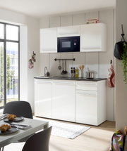 Moderne Single-Küche in Weiß mit Hängeschränken, eingebauter Mikrowelle und Spüle, aus der Perspektive eines Essbereichs mit Tisch und Stühlen.
