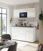 Moderne Single-Küche in Weiß mit Hängeschränken, eingebauter Mikrowelle und Spüle, aus der Perspektive eines Essbereichs mit Tisch und Stühlen.