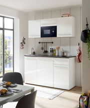 Moderne Single-Küche in Weiß mit Hängeschränken, eingebauter Mikrowelle und Spüle, aus der Perspektive eines Essbereichs mit Tisch und Stühlen.