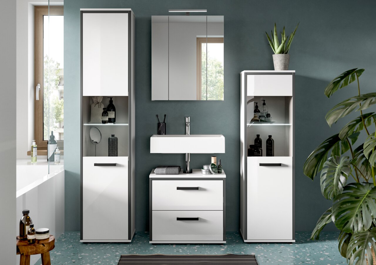 Frontale Ansicht eines modernen weißen Badmöbel-Sets mit Waschtischunterschrank, Spiegel-/Spiegelschrank und zwei Hochschränken mit Glasablagen und LED-Beleuchtung vor dunkelgrüner Wand.