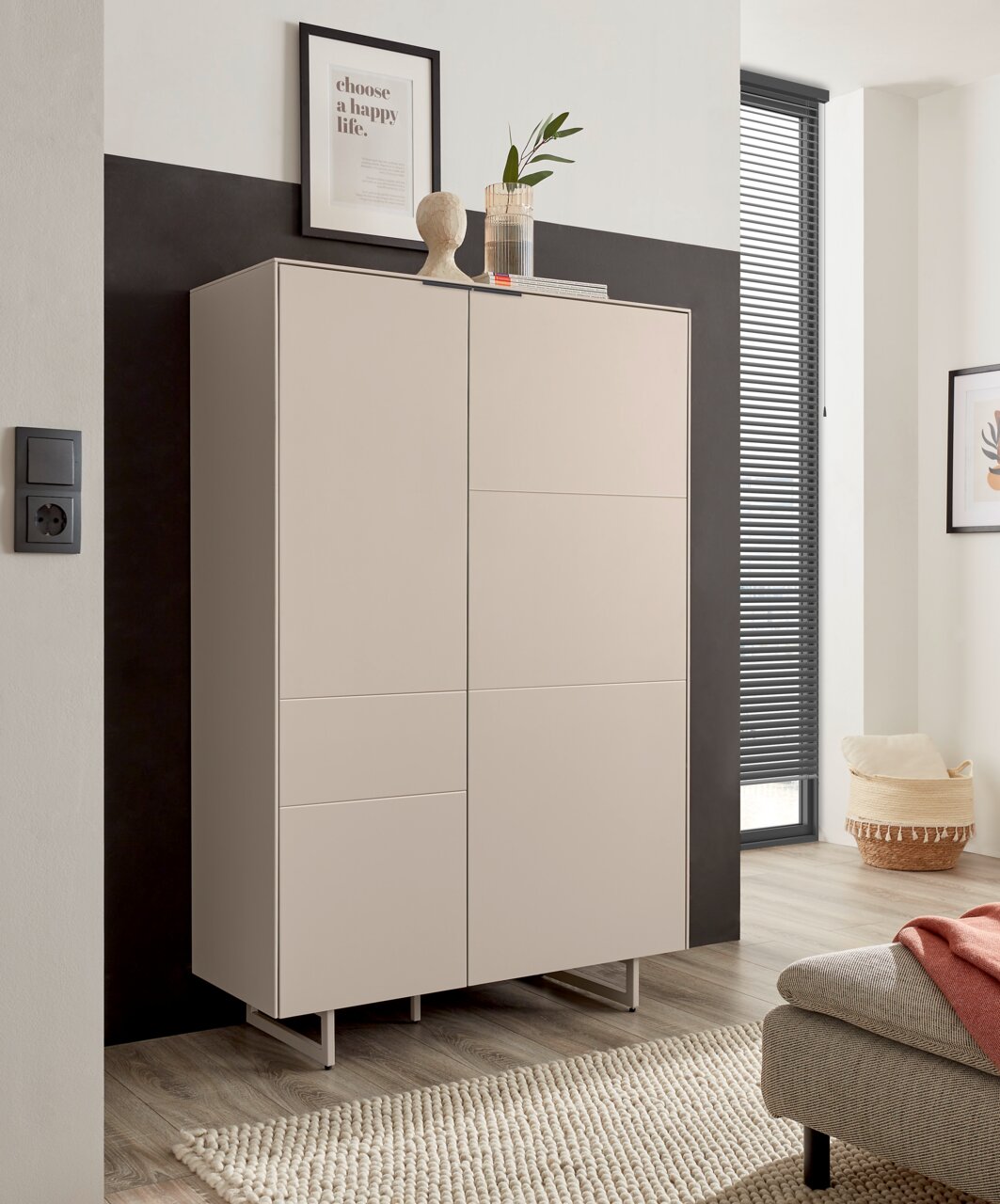 Een beige, moderne kast met twee gladde deuren en slanke metalen poten in een lichte woonkamer, van voren gefotografeerd vanuit een licht schuin perspectief.
