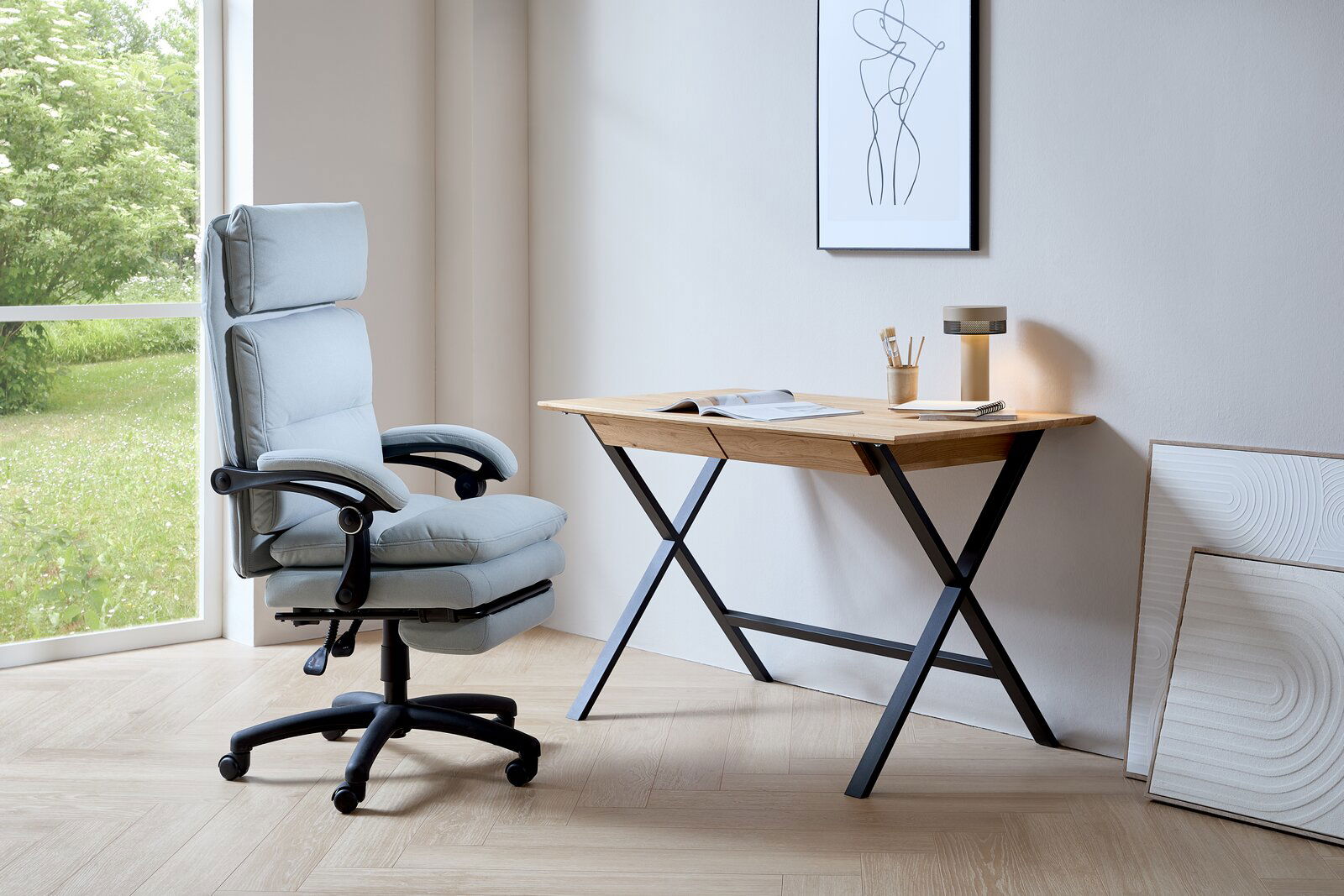 Venda Chefsessel ELIAS Moderner Chefsessel in hellblauem Stoff, seitliche Perspektive, neben einem Schreibtisch mit Holzplatte und schwarzem Metallgestell, in einem hellen Raum mit großem Fenster.