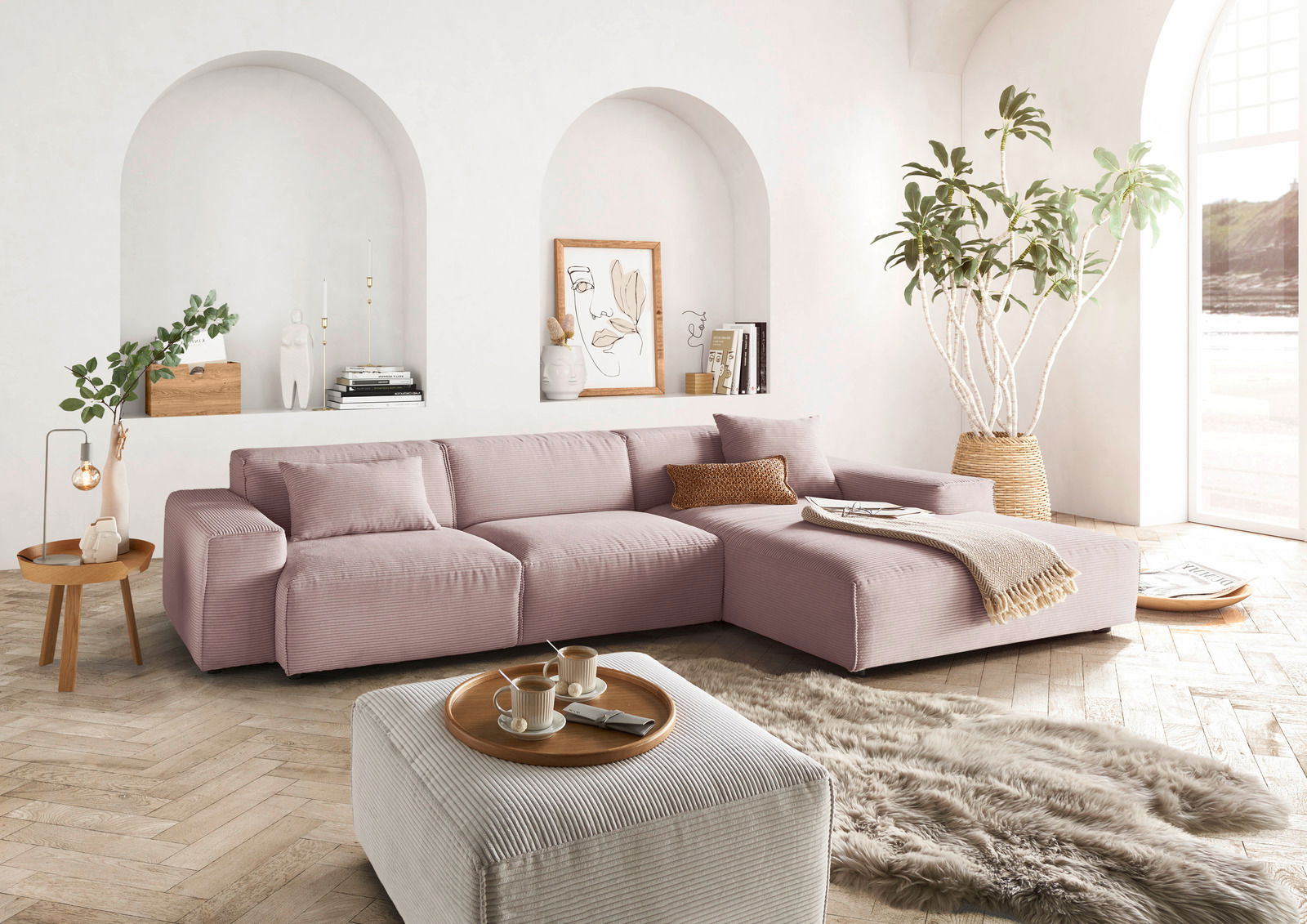 Lounge Handmade Hoekbank LH-EDINA Moderne, gemütliche Rundecke in einem hellen Wohnzimmer mit großen Fenstern, Pflanzen und stilvollen Dekorationen, aus der Perspektive von vorne rechts betrachtet.