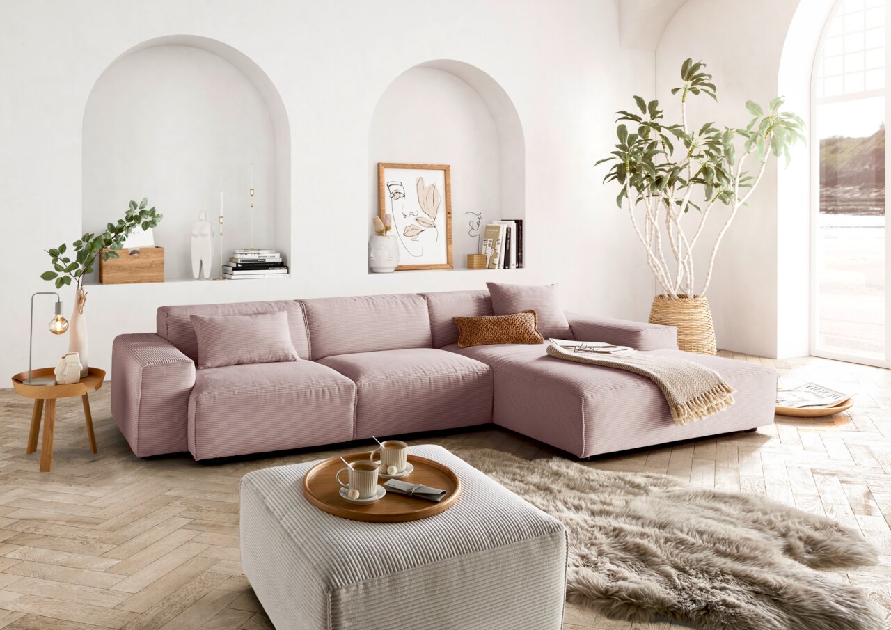 Lounge Handmade Ecksofa LH-EDINA Moderne, gemütliche Rundecke in einem hellen Wohnzimmer mit großen Fenstern, Pflanzen und stilvollen Dekorationen, aus der Perspektive von vorne rechts betrachtet.