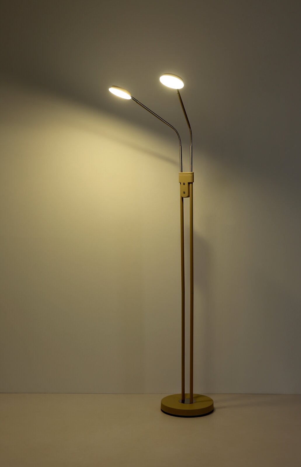 Moderne zweiflammige LED-Stehleuchte in Beige mit zwei verstellbaren, schlanken Armen und rundem Standfuß, eingeschaltet vor neutralem Hintergrund, Frontalansicht.