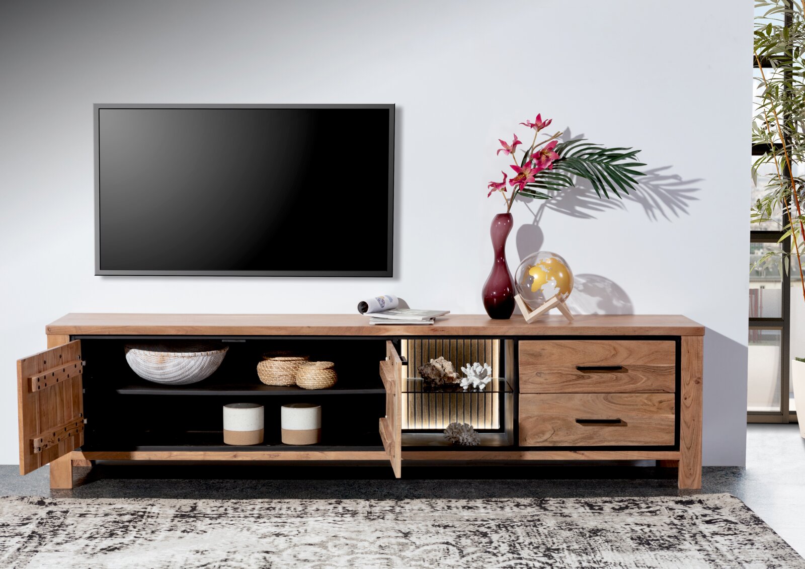 Vooraanzicht van een houten lowboard met open en gesloten vakken, versierd met vazen en een wereldbol, tegen een muur met een televisie.