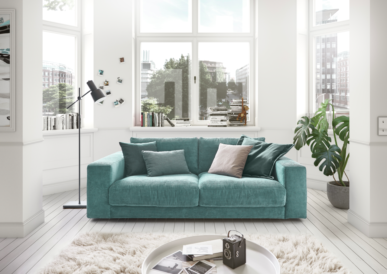 Lounge Handmade Sofa 2-Sitzer LH-SAMBIA Zweiersofa in einem modernen Wohnzimmer mit großen Fenstern, grünen Pflanzen und dekorativen Kissen, Frontalansicht.