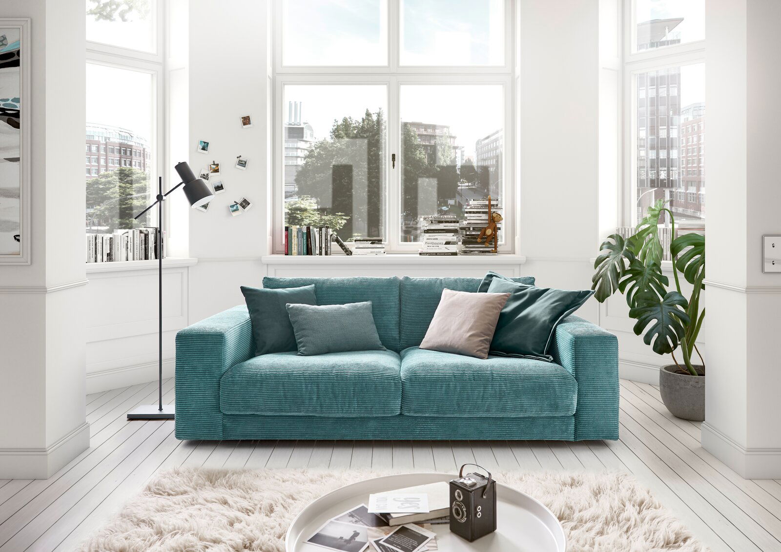 Zweiersofa in einem modernen Wohnzimmer mit großen Fenstern, grünen Pflanzen und dekorativen Kissen, Frontalansicht.