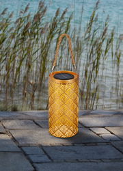 Solarbetriebene Laterne mit dekorativem Muster und Tragegriff, auf einer Terrasse mit Blick auf Schilf und Wasser.