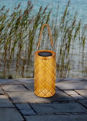 Zonne-energie-lantaarn met decoratief patroon en handvat, op een terras met uitzicht op riet en water.