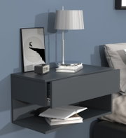 Moderne graublaue Wandkonsole/Nachttisch mit Schublade und Ablage, dekoriert mit Tischlampe, Bilderrahmen und Büchern, in seitlicher Perspektive leicht von vorne.