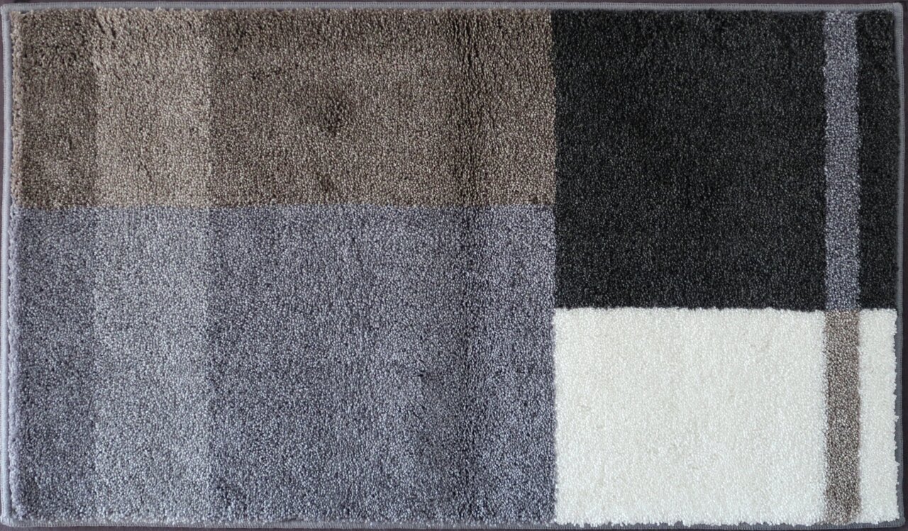 Badteppich in rechteckiger Form mit geometrischem Muster in verschiedenen Grautönen und Weiß, aus der Vogelperspektive fotografiert.