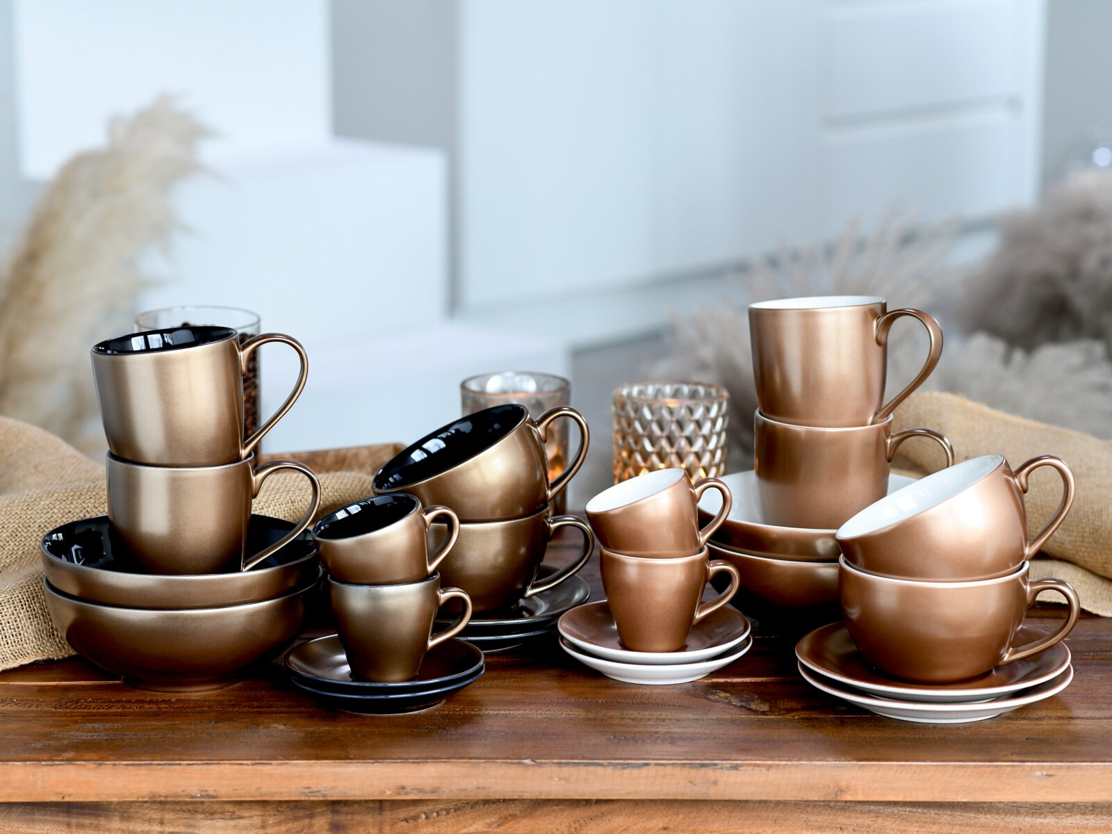 Creatable Espressoset 4-tlg GOLDEN DAYS Bronzefarbenes Geschirr-Set mit Tassen, Untertassen, Schalen und Tellern auf Holztisch arrangiert, aufgenommen in leicht schräger Vorderansicht.