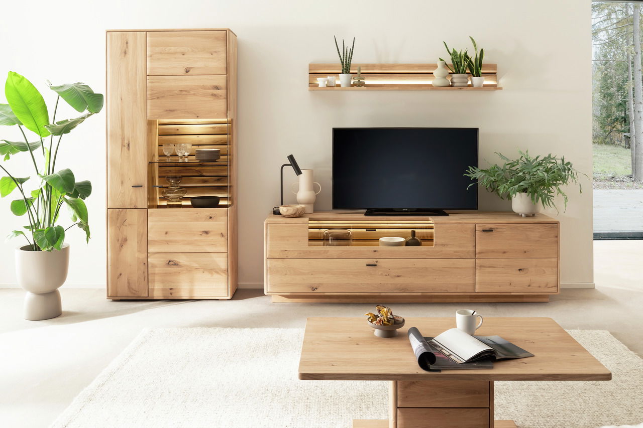 Linea Natura Wandkombination GEORGIA Moderne Wandkombination aus Holz mit TV-Schrank, Regal und Vitrine, frontal fotografiert in einem hellen Wohnzimmer mit Pflanzen.
