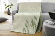Jacquard Decke in Grün- und Beigetönen mit Pflanzenmuster, drapiert über einem grauen Sofa in einem modernen Wohnzimmer.
