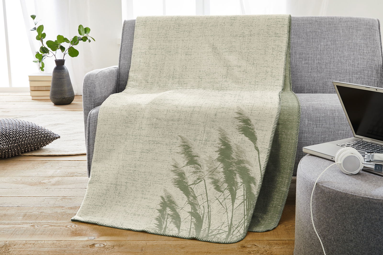 Jacquard Decke in Grün- und Beigetönen mit Pflanzenmuster, drapiert über einem grauen Sofa in einem modernen Wohnzimmer.