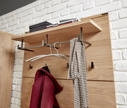 Garderobenpaneel aus Holz mit Metallhaken, von schräg vorne fotografiert. Oben befindet sich ein Regalbrett mit Büchern und einer Box, darunter hängen ein roter Mantel und ein Schal.