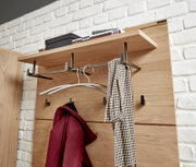 Garderobenpaneel aus Holz mit Metallhaken, von schräg vorne fotografiert. Oben befindet sich ein Regalbrett mit Büchern und einer Box, darunter hängen ein roter Mantel und ein Schal.