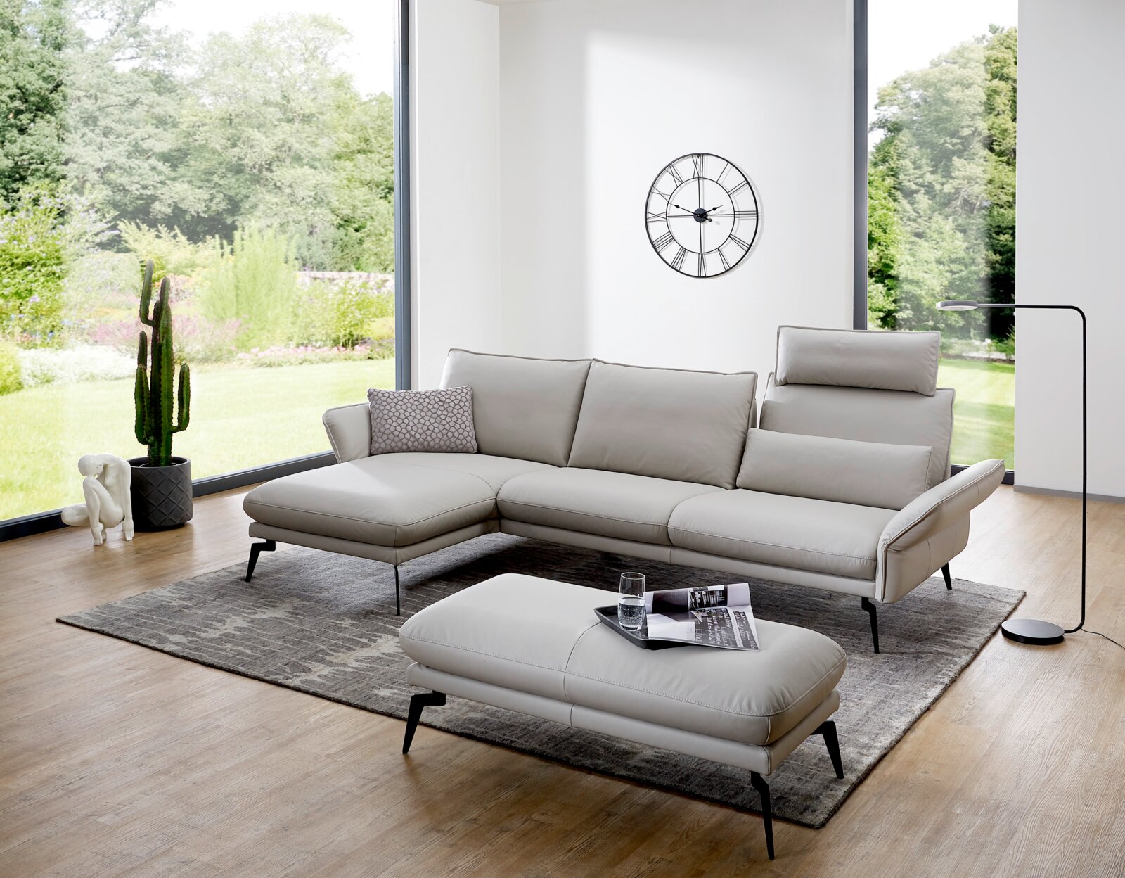 Moderne Longchairkombination in einem hellen Wohnzimmer mit großen Fenstern, grauem Teppich und stilvoller Dekoration. Perspektive von vorne links.