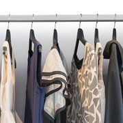 Kleding aan zwarte hangers aan een metalen kledingstang, met jurken en blouses in wit, blauw en zwart met patronen, gefotografeerd van voren op ooghoogte.