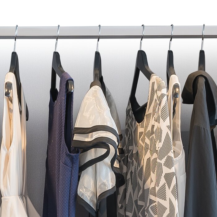 Kleding aan zwarte hangers aan een metalen kledingstang, met jurken en blouses in wit, blauw en zwart met patronen, gefotografeerd van voren op ooghoogte.