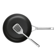 Schwarze Bratpfanne mit Edelstahlgriff und Edelstahl-Schlitzwender, Draufsicht von oben auf weißem Hintergrund