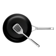 Schwarze Bratpfanne mit Edelstahlgriff und Edelstahl-Schlitzwender, Draufsicht von oben auf weißem Hintergrund