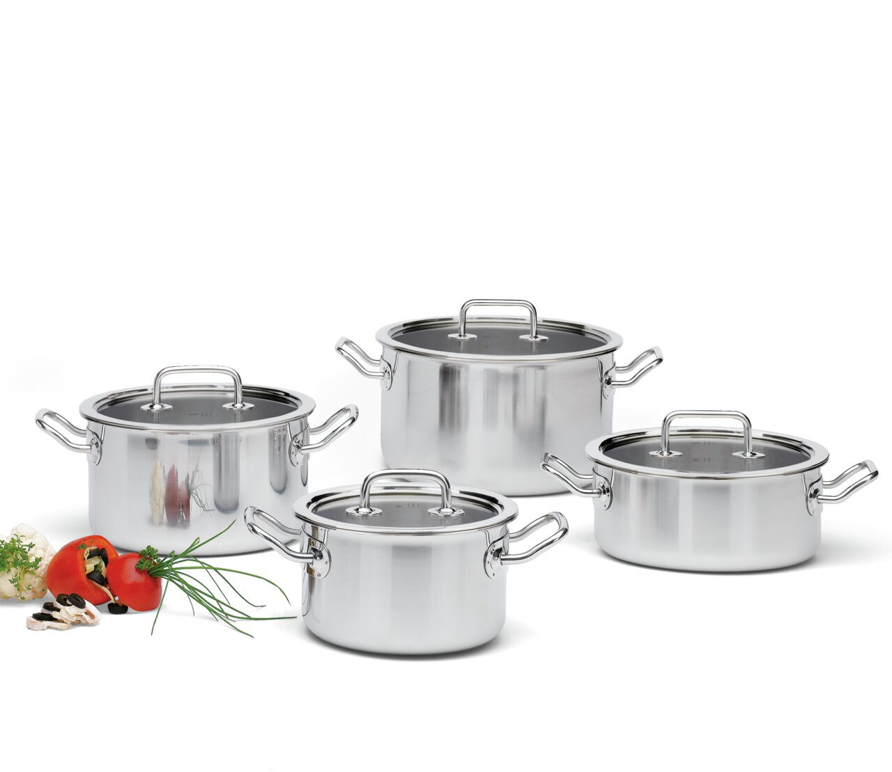 Vier-teiliges Topf-Set Brigade Basic aus Edelstahl, frontal fotografiert, mit Glasdeckeln und seitlichen Griffen, umgeben von frischen Zutaten wie Tomaten und Kräutern.