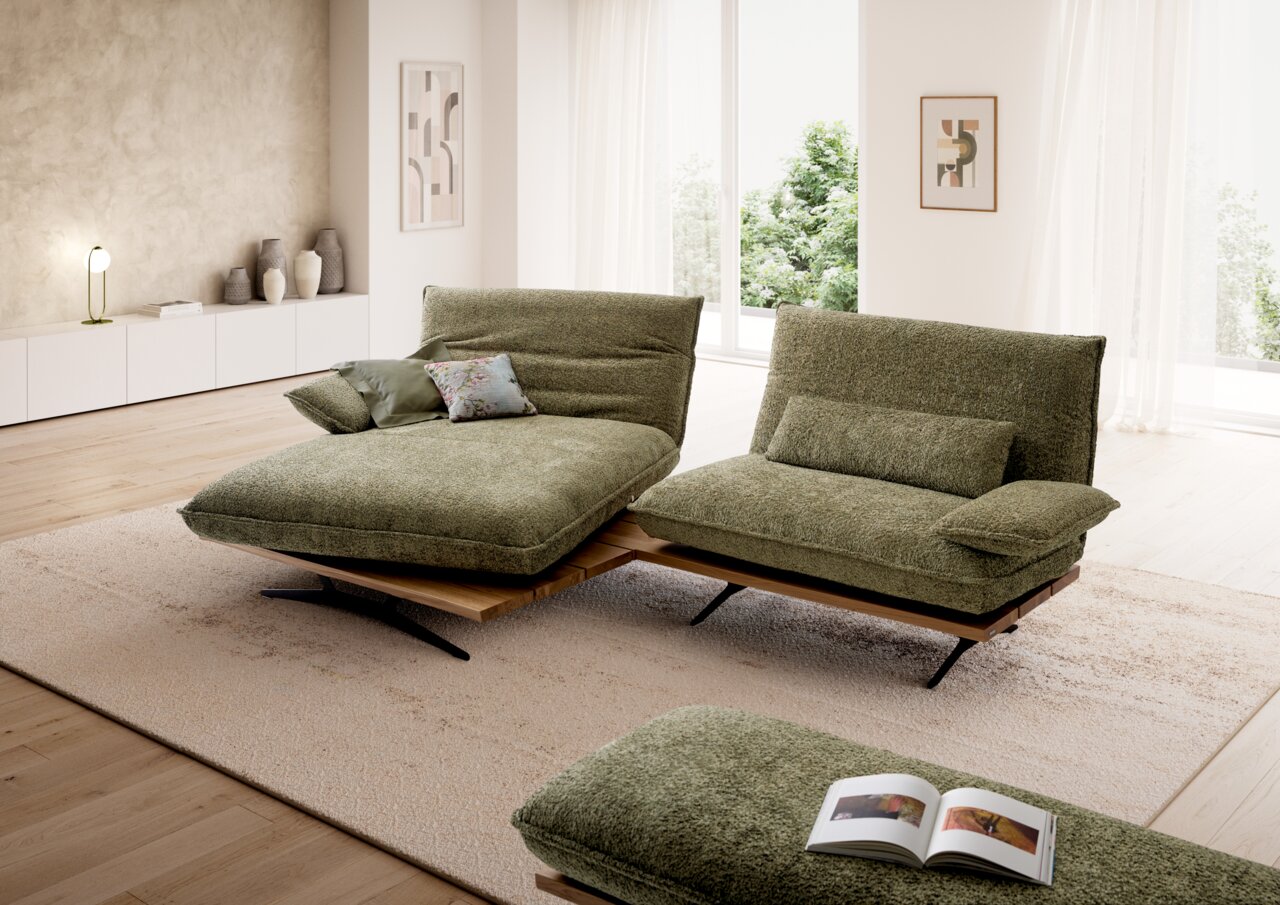 Moderne groene gestoffeerde bankstel met chaise longue en tweezitsbank op een houten sokkel met zwarte metalen poten in een lichte woonkamer, vooraanzicht in licht schuin perspectief