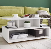Weißer, moderner Couchtisch mit Ablagefächern vor grünem Sofa, dekoriert mit zwei Tassen, Schale mit Kirschen, Büchern, Pflanze und Korb, in frontaler leicht erhöhter Perspektive.