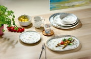 Florales Geschirrset aus weißer Keramik mit Tellern, Schalen und Tasse, dekorativ auf einem Holztisch arrangiert, aus schräger Vogelperspektive