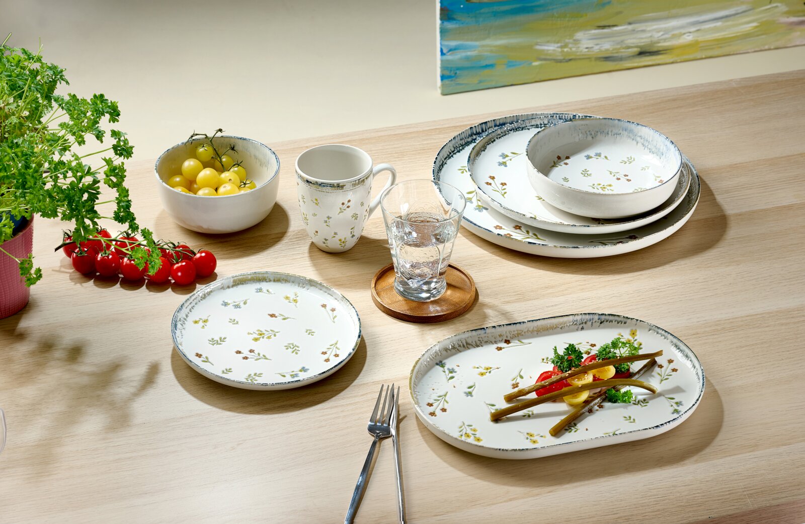 Florales Geschirrset aus weißer Keramik mit Tellern, Schalen und Tasse, dekorativ auf einem Holztisch arrangiert, aus schräger Vogelperspektive