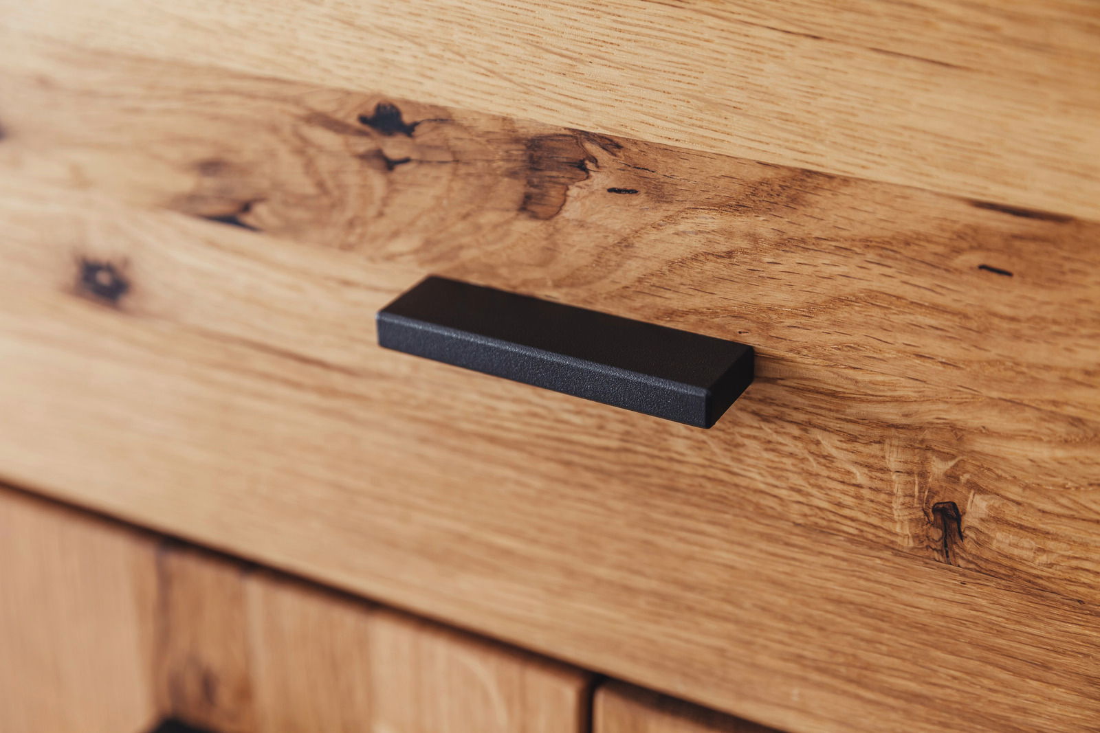 Nahaufnahme eines Holzschranks mit einer schwarzen Griffleiste, die eine elegante und moderne Optik verleiht.