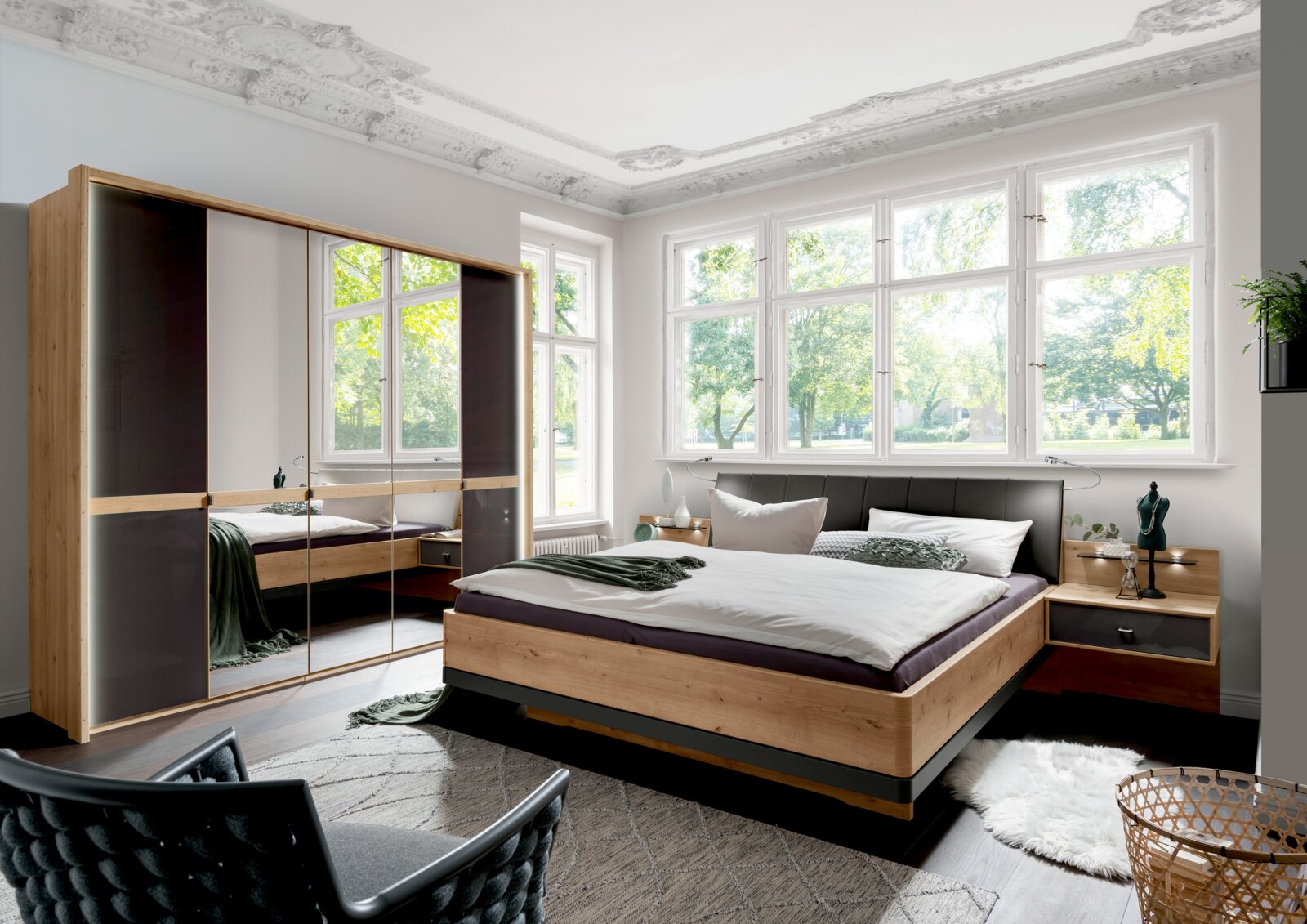 Modern houten futonbed met gestoffeerd hoofdeinde in een lichte slaapkamer met grote ramen, gezien vanaf de zijkant.