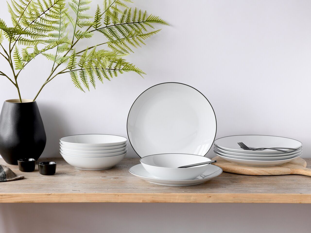 Tafelservice 12-tlg. Luna Black, bestehend aus weißen Tellern und Schalen mit schwarzem Rand, auf einem Holztisch arrangiert, seitliche Perspektive.