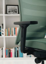 Seitenansicht eines grünen Bürostuhls mit Armlehne vor einem Bücherregal