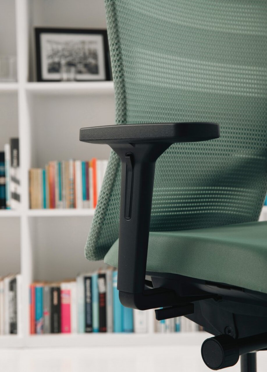 Seitenansicht eines grünen Bürostuhls mit Armlehne vor einem Bücherregal