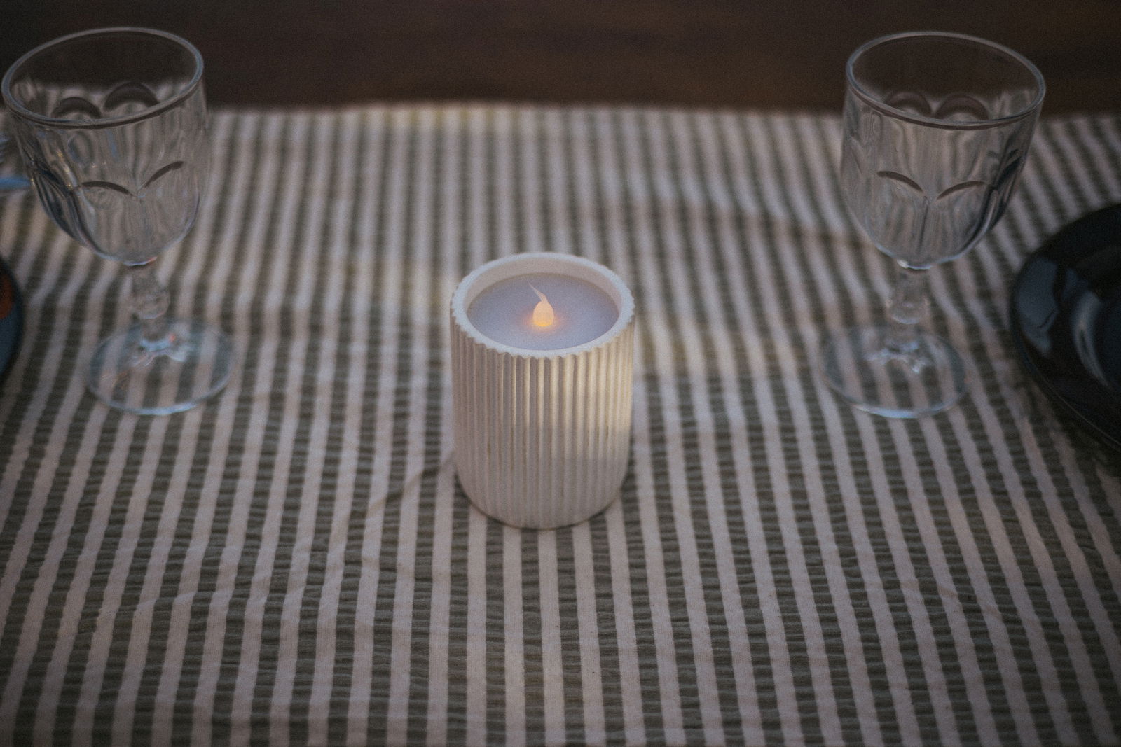 Outdoor-Kerze auf einem gestreiften Tischtuch, umgeben von zwei Weingläsern, aus der Vogelperspektive fotografiert.